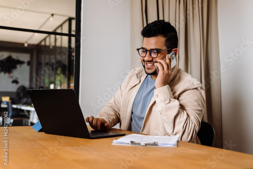 Smiling business man talking on mobile phone while working in office