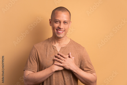 happy bald man hands over heart, chest in beige colors. care, love, affection, support concept.