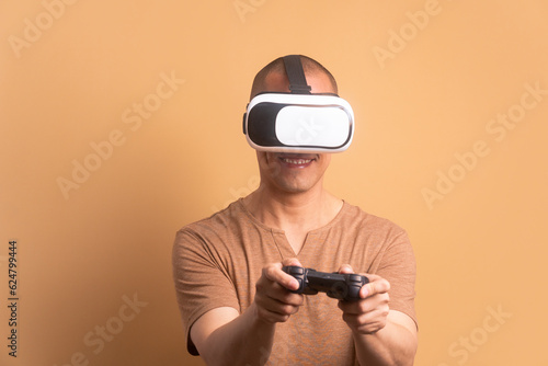 cheerful brazilian man playing videogame with VR headset in beige studio background. virtual reality, gaming, leisure concept.