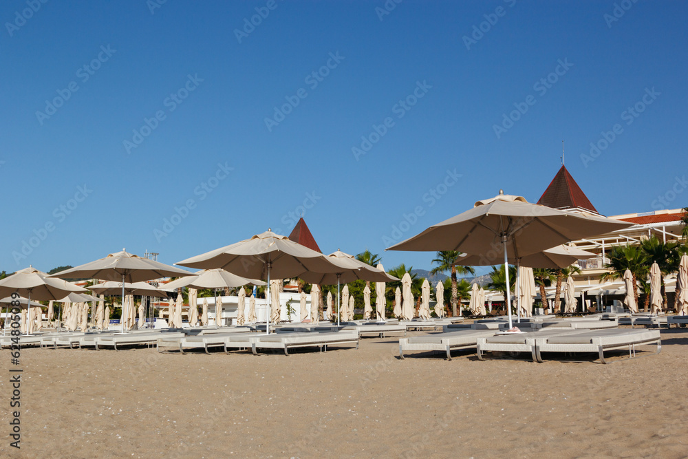Row of sun loungers and umbrellas on the empty beach during sunrise awaits tourists. Blue sky background