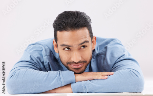 Thinking, dreaming and young man in a studio resting on his arms with a contemplating facial expression. Happy, smile and Indian male model with question or remember face isolated by white background © Nadia L/peopleimages.com