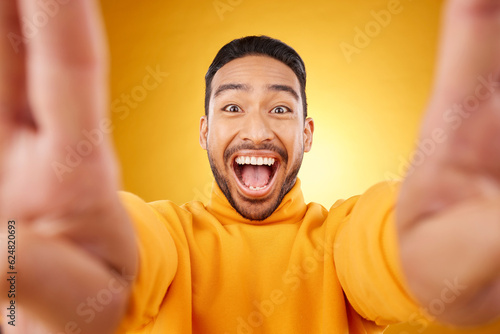 Funny, portrait and selfie of excited man in studio isolated on a yellow background. Face, smile and Asian person taking profile picture for happy memory, laughing and photography on social media