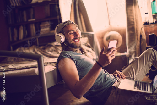Young man using a smart phone and laptop whie listening to music in the bedroom