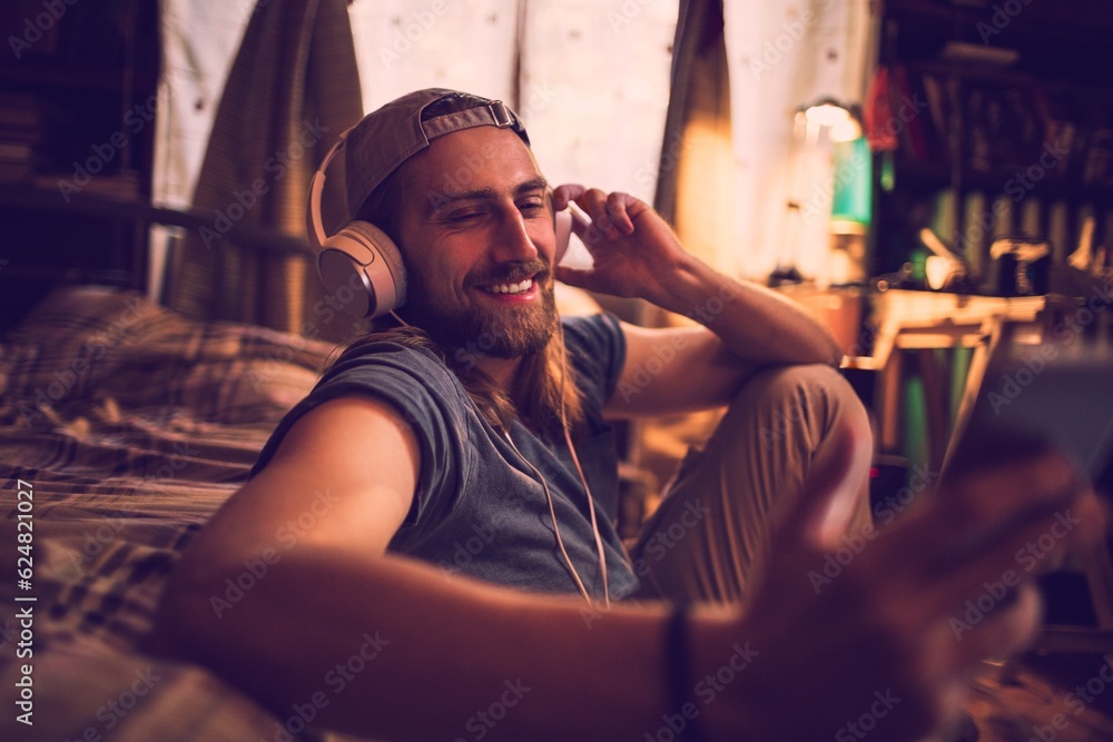 Young man listening to music on his smart phone while sitting in his bedroom