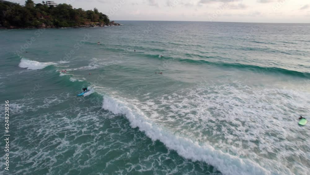 Paddle surfing near the beach at sunset. The view from the drone. Small waves create foam. The guy is flying on a board to the shore. Water reflects the rays of the sun. People are bathing. Phuket Paddle surfing near the beach at sunset. The view from the drone. Small waves create foam. The guy is flying on a board to the shore. Water reflects the rays of the sun. People are bathing. Phuket