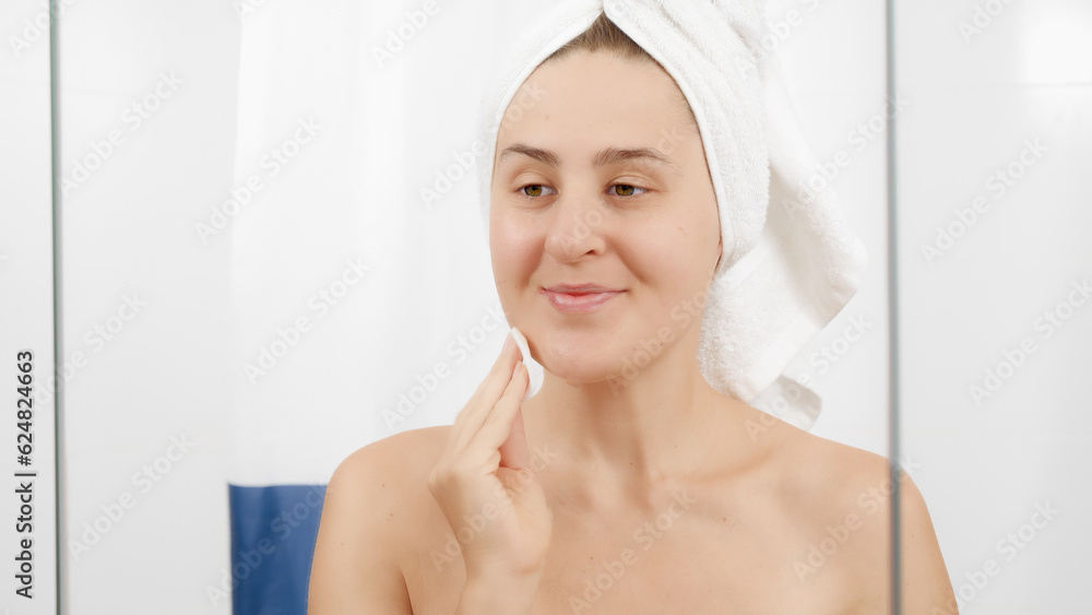 Young woman cleaning face with cotton pad and cleanser in bathroom. Concept of beautiful female, makeup at home, skin care and domestic beauty industry Young woman cleaning face with cotton pad and cleanser in bathroom. Concept of beautiful female, makeup at home, skin care and domestic beauty industry