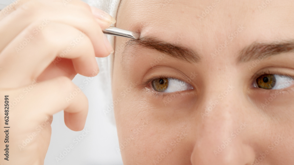 Closeup portrait of smiling young woman forming eyebrows with tweezers after having bath. Concept of beautiful female, makeup at home, skin care and domestic beauty industry.