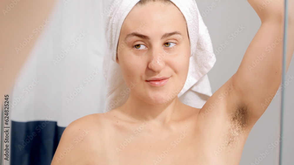 Young smiling woman lifting her arm and looking on long armpit hair after having shower. Concept of beautiful female, natural beauty, feminity and body hair. Young smiling woman lifting her arm and looking on long armpit hair after having shower. Concept of beautiful female, natural beauty, feminity and body hair.