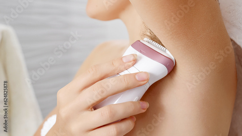 Fotografía Young woman using electric epilator to remove armpit hair in bathroom