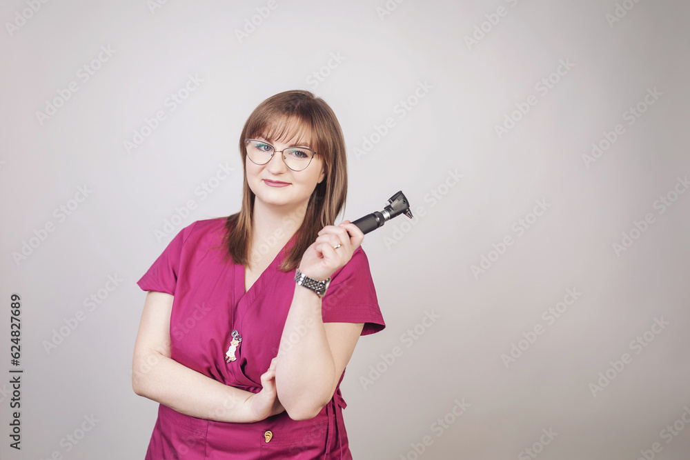 A young smiling ORL doctor. Woman Audiologist with otoscope on grey background. Ear treatment and hear exam. Female otolaryngologist with otoscope. Medicine and healthcare concept. A young smiling ORL doctor. Woman Audiologist with otoscope on grey background. Ear treatment and hear exam. Female otolaryngologist with otoscope. Medicine and healthcare concept.