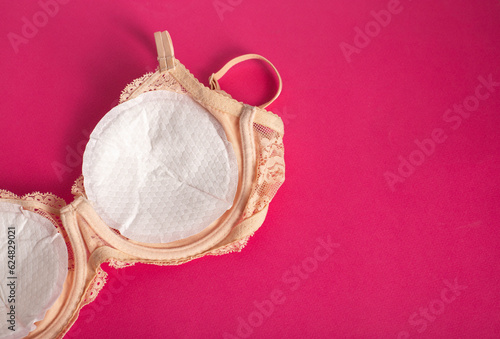 Women's bra with liners against the flow of milk from the breast of a nursing woman on a pink background. Copy space for text photo
