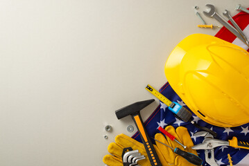 Labor Day tribute: A captivating top-view image showcasing the American flag, construction helmet, work gloves, and tools on a light grey background. Perfect for Labor Day promotions or text placement