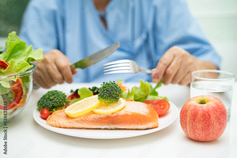 Asian elderly woman patient eating salmon steak breakfast with vegetable healthy food in hospital.