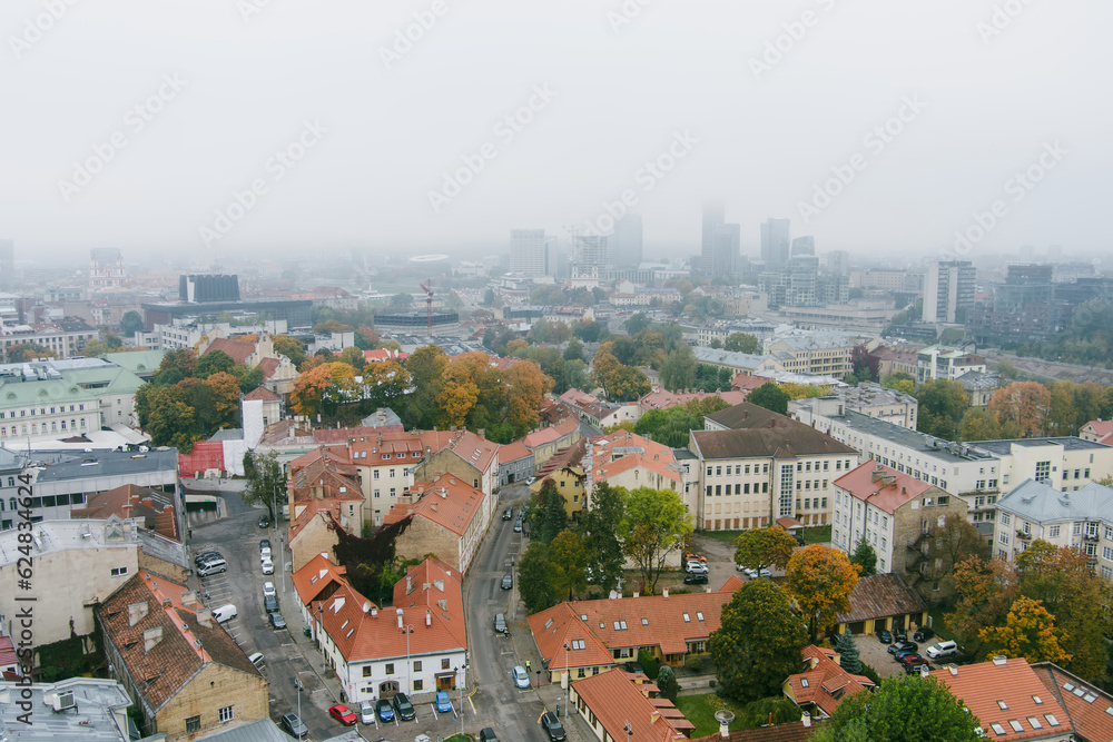 Beautiful foggy Vilnius city scene in autumn with orange and yellow foliage. Aerial early morning view.