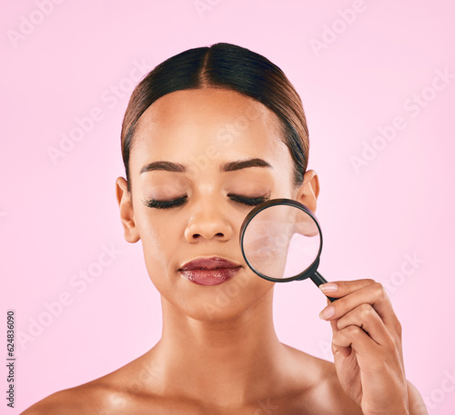 Woman, face and magnifying glass, beauty and zoom in on pores, skincare and makeup isolated on pink background. Search, investigate and check skin with glow, female model and dermatology in studio