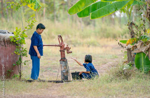 Asian boy use groundwater lever to get water for little girl and they look happy to get fresh water.