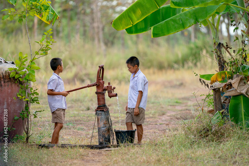 Two Asian boys use groundwater lever to get water for clean and also to grow some plants in the field.