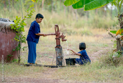 Asian boy use groundwater lever to get water for little girl and they look happy to get fresh water.