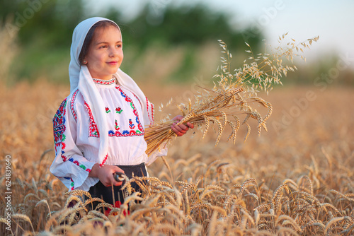 bulgarian woman little girl in ethnic folklore costume hold golden wheat straws and sickle in harvest field, harvesting and agriculture in Bulgaria photo