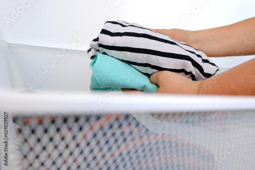 bunch of colorful clothes, woman housewife cleaning room, female hands lays out women's clothes, textiles, knitwear in white mesh metal basket in modern bedroom, minimalism, simplicity