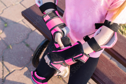 Protective pink oversleeves in the girl's arms. The concept of protection against injuries during falls while riding a scooter, roller skates and a bicycle. photo