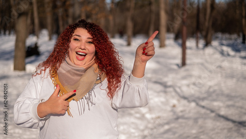 A chubby red-haired woman in a white sweatshirt. Girl fooling around in the park in winter. 