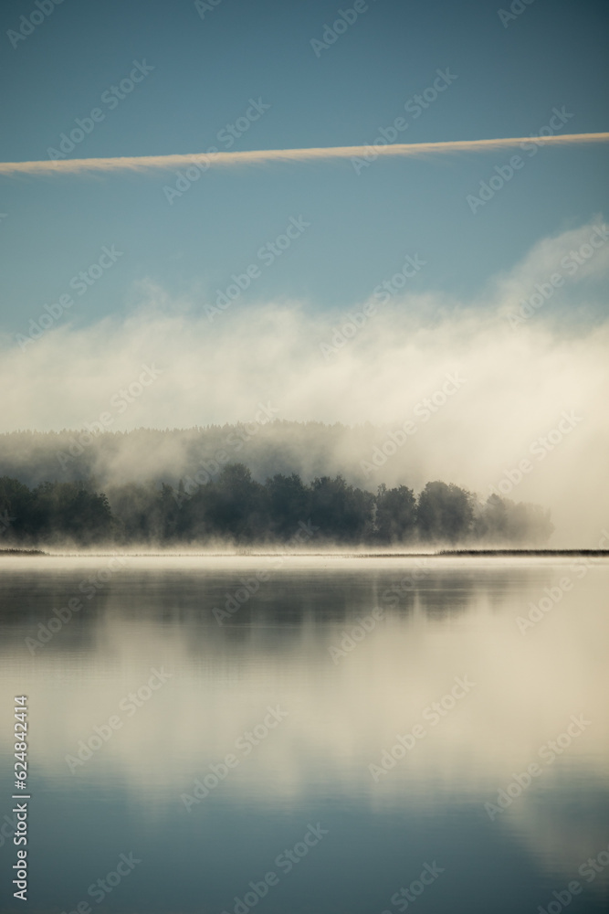 Misty morning on top of a still reflecting lake.