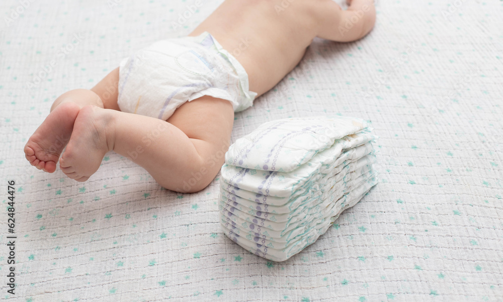 © HENADZY - The legs of a baby in a diaper against the background of a stack of children's comfortable diapers, close-up. Copy space for text © HENADZY - The legs of a baby in a diaper against the background of a stack of children's comfortable diapers, close-up. Copy space for text
