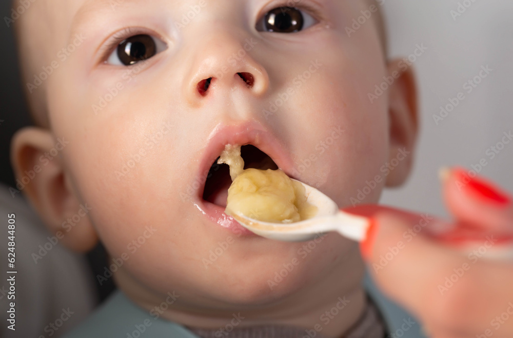 The first feeding with fruit puree for a baby boy who is 6 months old, close-up The first feeding with fruit puree for a baby boy who is 6 months old, close-up