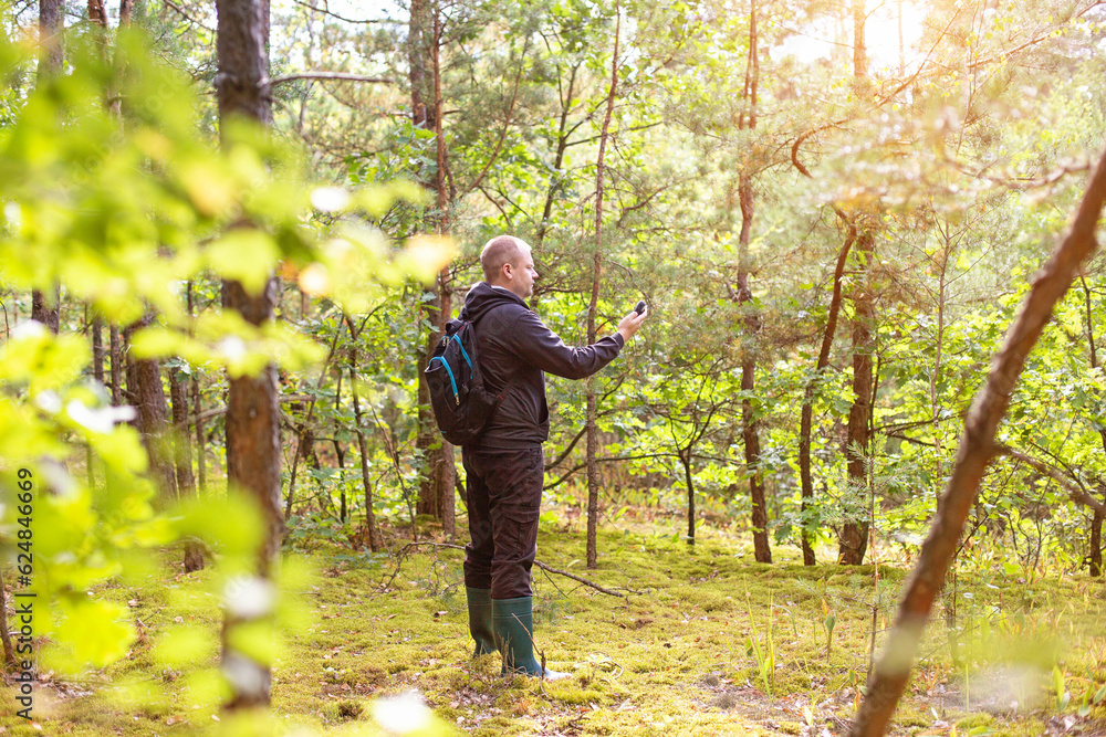 A man in the forest with a navigator in his hand. Location determination. The mushroom picker got lost in the forest. Compass and survival. Copy space for text, sunshine A man in the forest with a navigator in his hand. Location determination. The mushroom picker got lost in the forest. Compass and survival. Copy space for text, sunshine