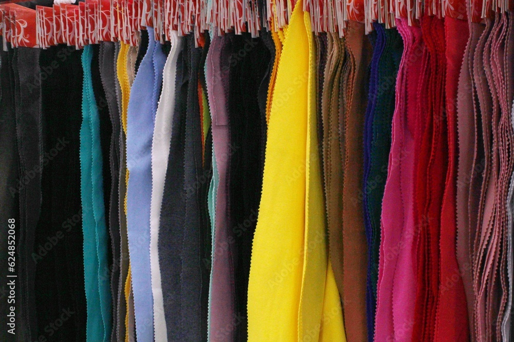 Colored textile samples of furniture and clothing upholstery of a fabric in shop. Close-up palette of texture vertical stripes on hangers. Fashion industry concept. Sewing materials. Embroidering