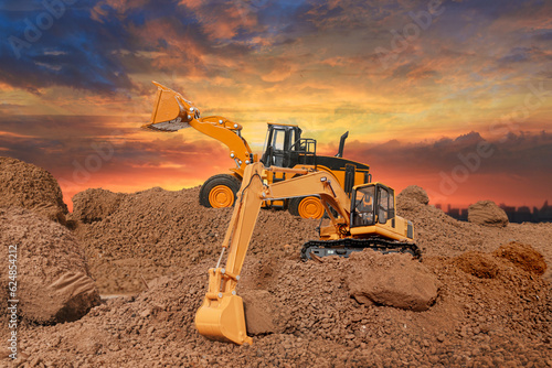 Wheel loader and Crawler excavator are digging the soil in the construction site. on the sunset background