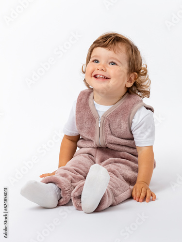 A happy contented kid, a toddler of 1-2 years old, is sitting on the floor in a lilac plush suit, smiling and looking up attentively. Copy space. Photo.