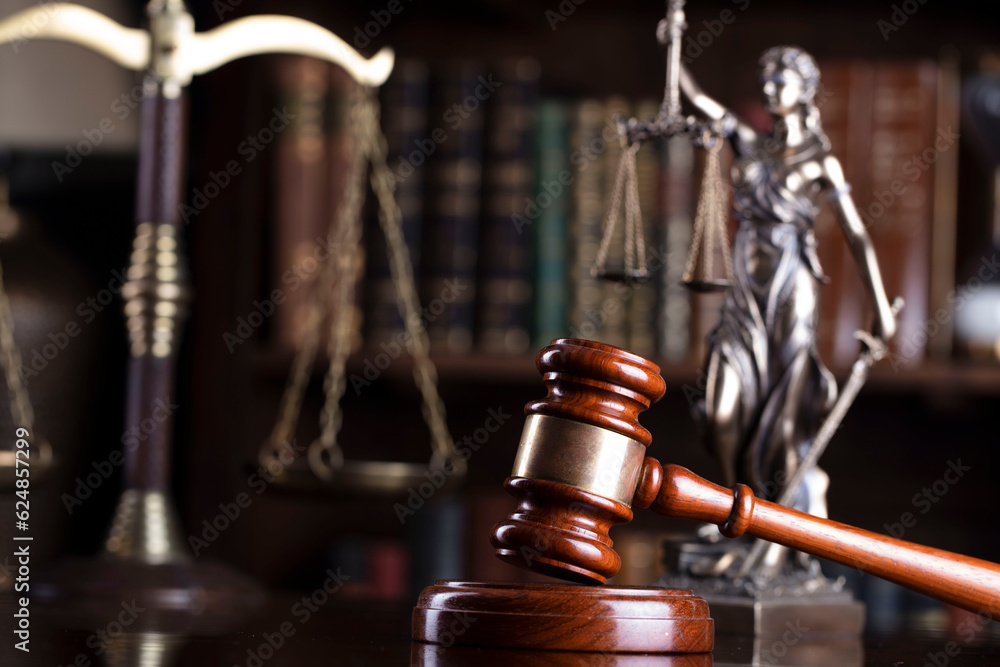 Lawyer office. Law symbols composition: judge’s gavel, scale and Themis sculpture on the brown shining desk. Bookcase with legal books in the background. Lawyer office. Law symbols composition: judge’s gavel, scale and Themis sculpture on the brown shining desk. Bookcase with legal books in the background.
