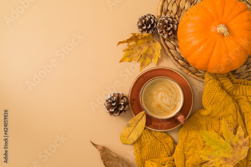Autumn season concept with coffee cup, warm sweater, fall leaves and pumpkin on beige background. Top view, flat lay