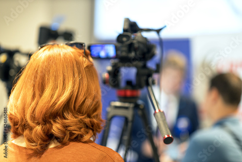 Camerawoman filming media event or press conference with a video or television camera. Public relations - PR concept.