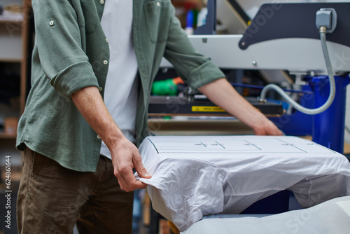 Foto Cropped view of young craftsman holding t-shirt with marking while working with