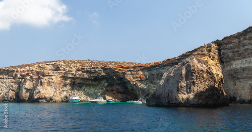 Pleasure boats sails near coastal caves at Blue Lagoon, Malta