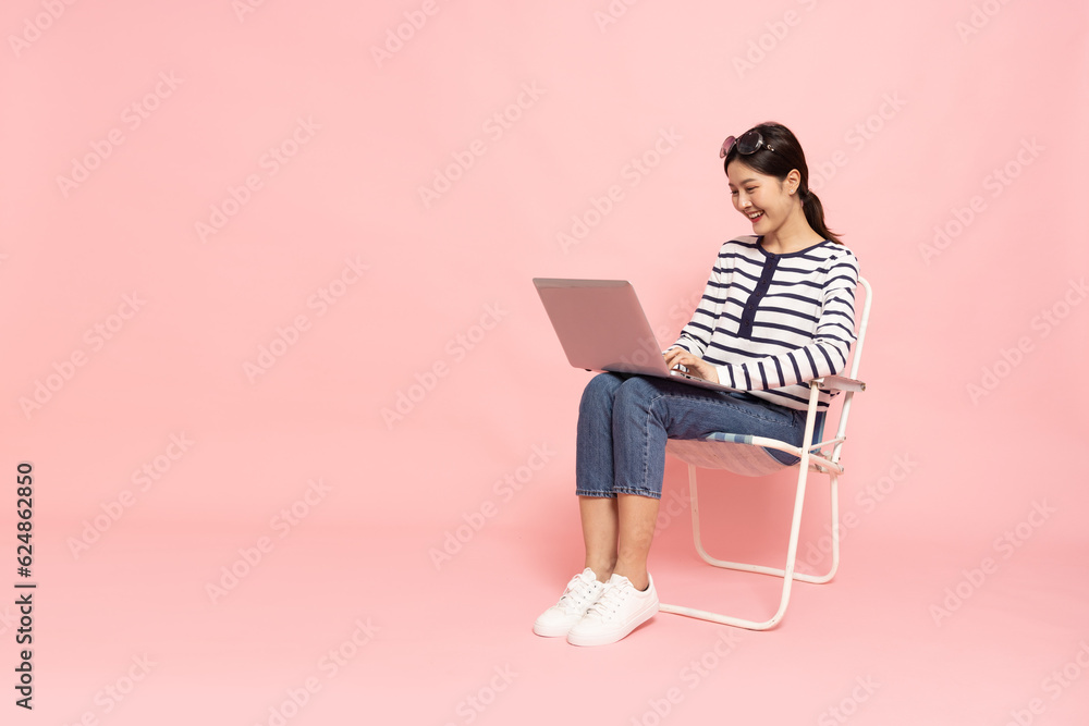 Portrait of an excited Asian woman sitting and typing keyboard on laptop computer isolated on pink background, Feeling happiness, Full body composition Portrait of an excited Asian woman sitting and typing keyboard on laptop computer isolated on pink background, Feeling happiness, Full body composition