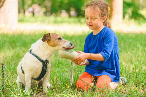 On hot summer day girl watering dog in park. Dog drinking water from special pet bottle. photo