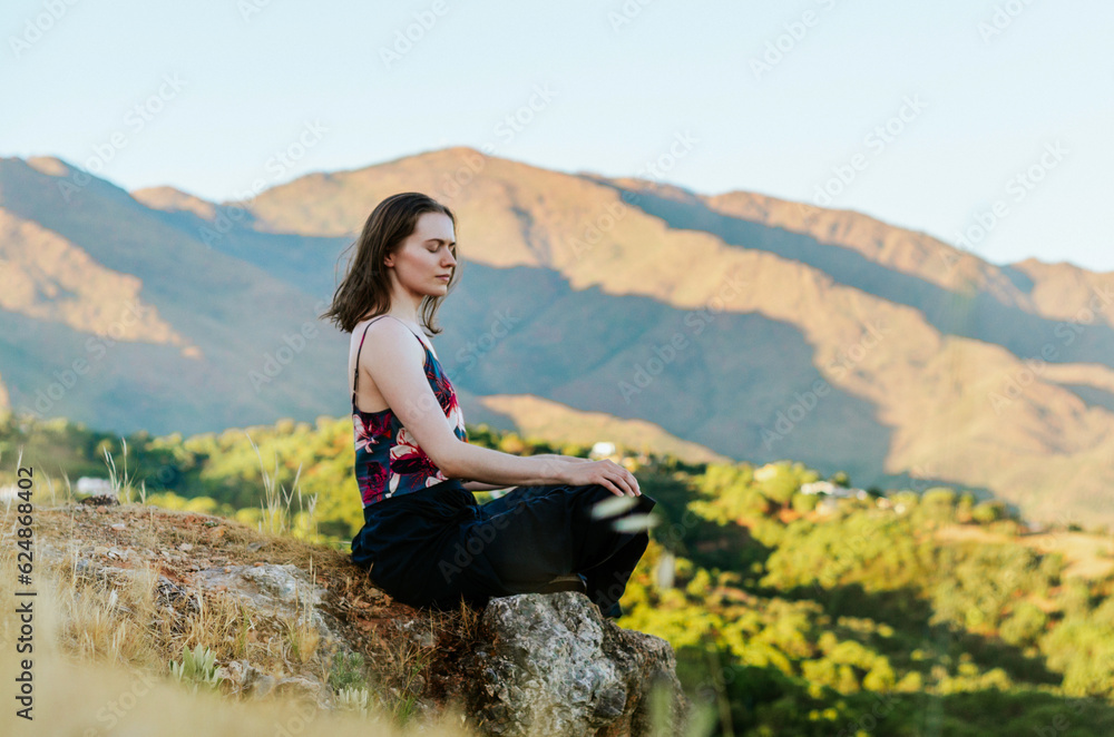 Woman sitting on a rock surrounded by mountains at sunset