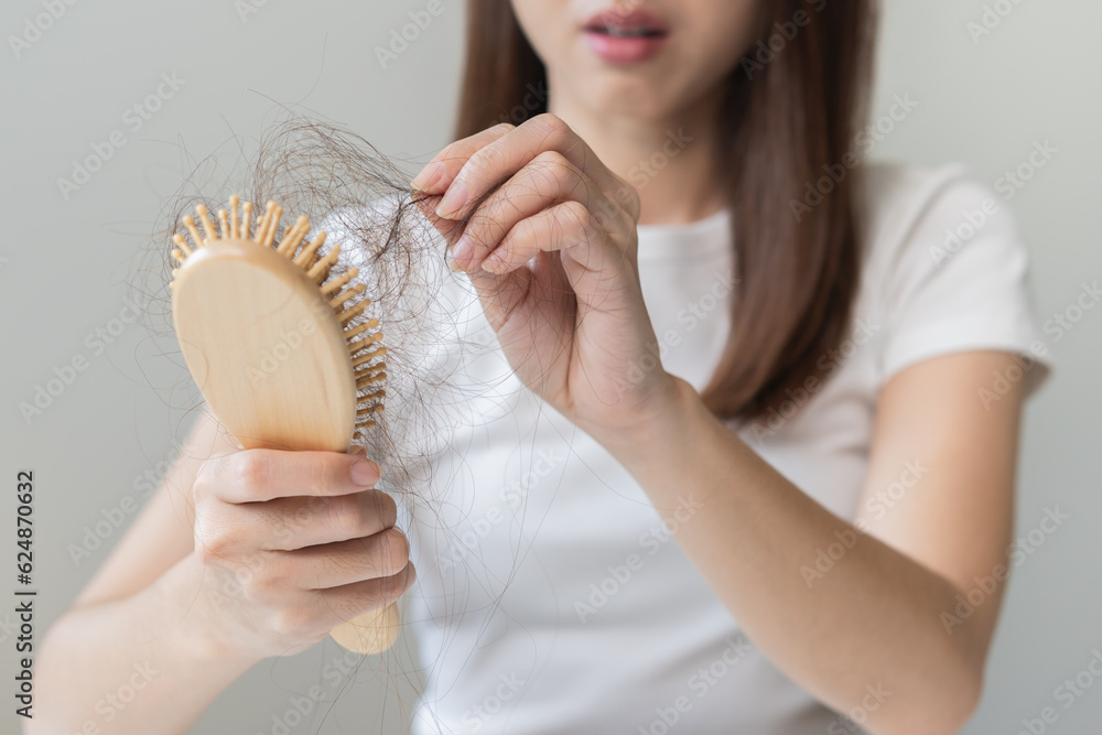 Serious asian young woman holding brush holding comb, hairbrush with fall black hair from scalp after brushing, looking on hand worry about balding. Health care, beauty treatment, hair loss problem. Serious asian young woman holding brush holding comb, hairbrush with fall black hair from scalp after brushing, looking on hand worry about balding. Health care, beauty treatment, hair loss problem.