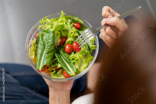 Top view happy meal eating healthy breakfast in morning, asian young woman, girl having fresh salad, tomato, green cos lettuce in bowl, sitting on floor in kitchen. Dieting, vegetarian food concept.