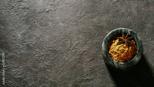 Fototapeta Naklejka Na Ścianę i Meble -  Indian or pakistani masala powder in black marble bowl on black textured background. Small marble bowl with dry curry garam masala mix spices blend with copy space. Top view or flat lay.