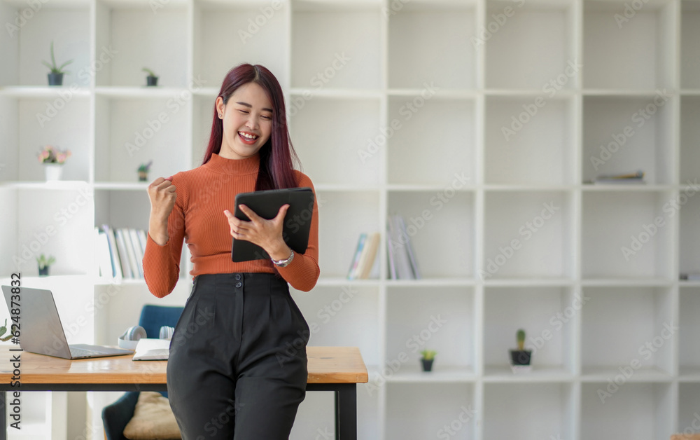 Asian Female using digital tablet and standing in the workplace. Victory while receiving good news Asian Female using digital tablet and standing in the workplace. Victory while receiving good news