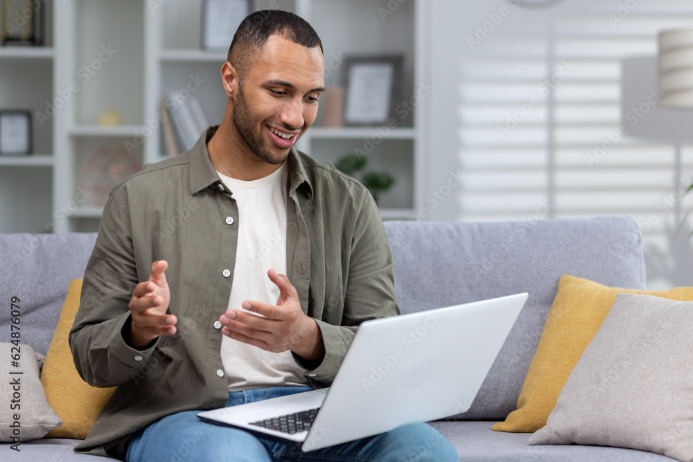 A young African American man is using a laptop. Sitting at home on the couch and talking online via video call A young African American man is using a laptop. Sitting at home on the couch and talking online via video call