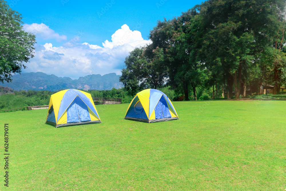 Two colorful tents placed on green lawn ground, tourism camping tents with wild nature panoramic view landscape of green forests and mountains.