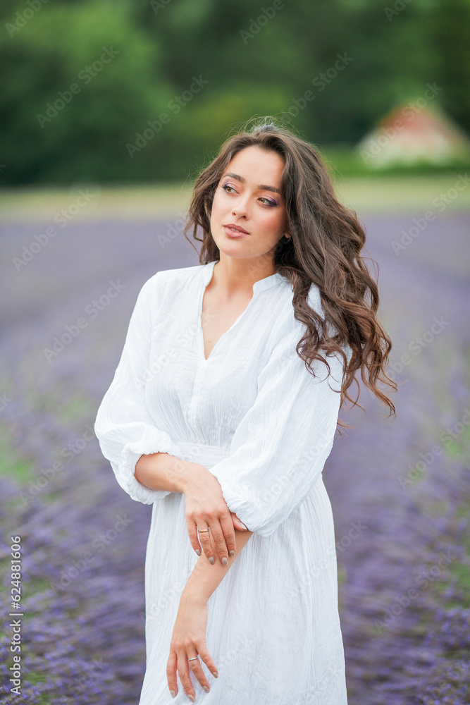 Lavender field. Beautiful dark-haired curly woman in white simple dress in field of purple flowers. Summer. Lavender field. Beautiful dark-haired curly woman in white simple dress in field of purple flowers. Summer.