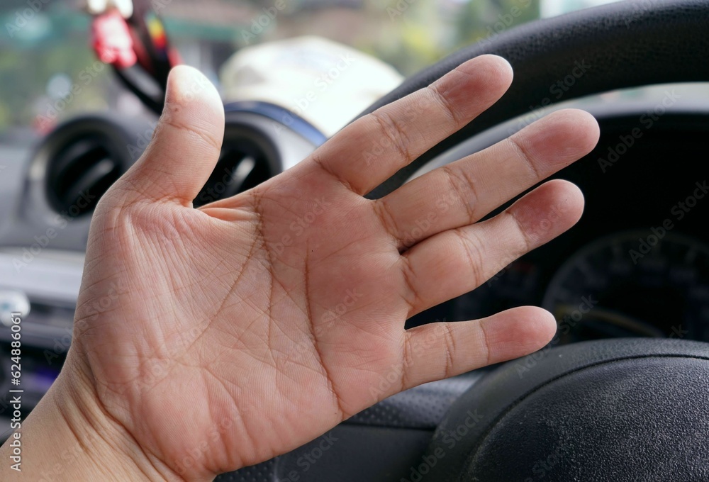 A hand on the steering wheel of a car, focus on hand.