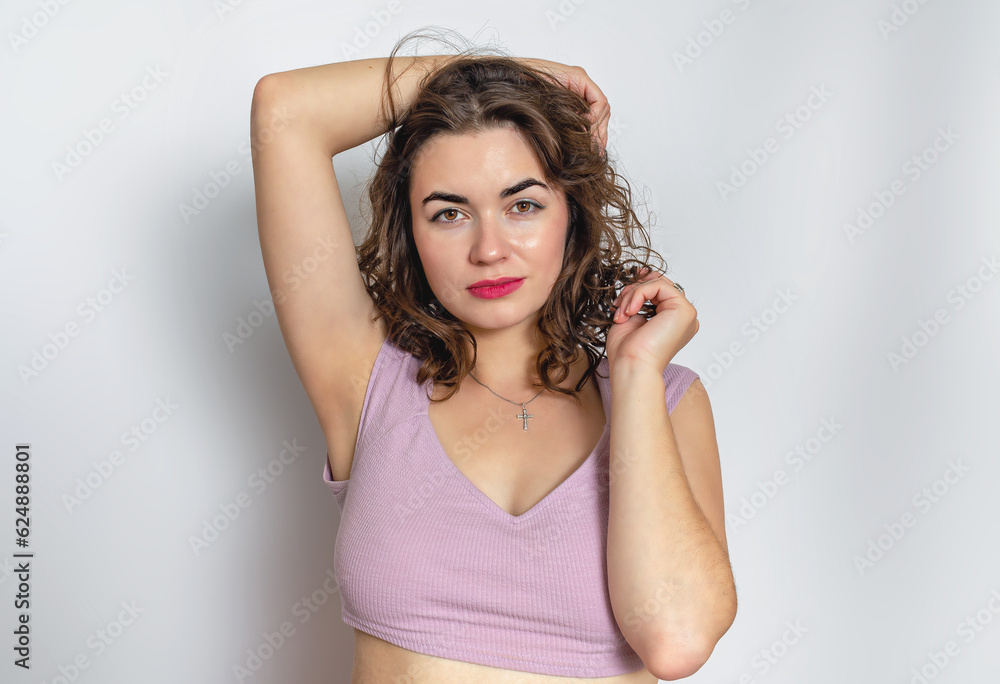 Fototapeta premium Playful mysterious brunette in a lilac top. She touches hair with her hand. Sexy look of brown eyes.